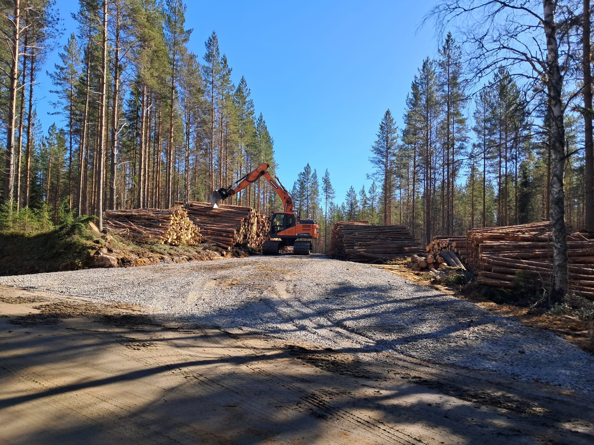 Kaivinkone metsätiellä puupinojen välissä