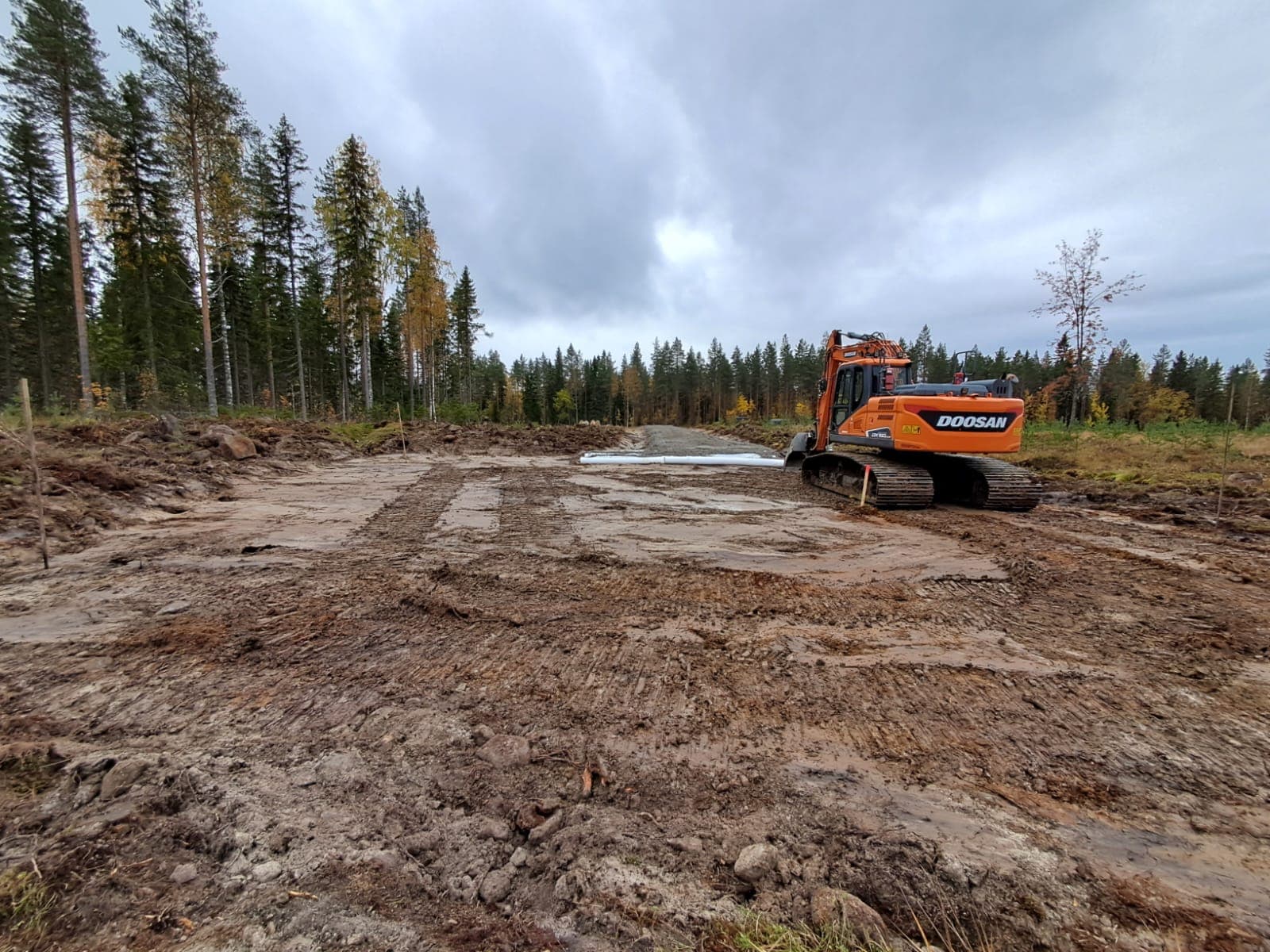Kaivinkone ja työstetty tiepohja metsässä.